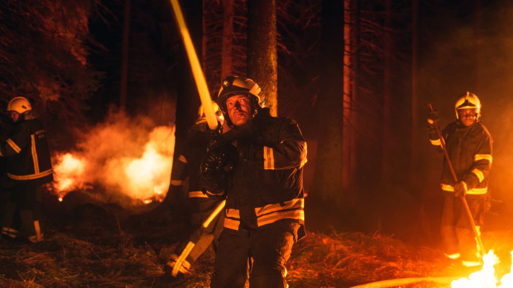 Professional Fireman in Safety Uniform and Helmet Spraying Water from Fire Hose to Battle the Wildfire.