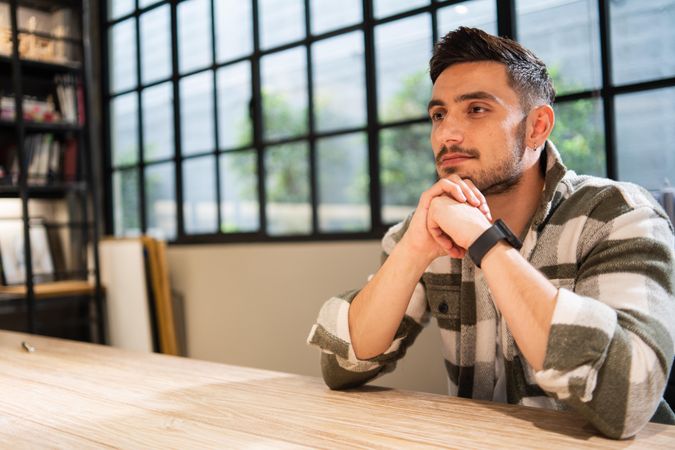 Man in bright office sitting at table deep in thought