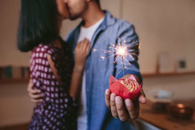 Young man holding cupcake with sparkler as he kisses his girlfriend