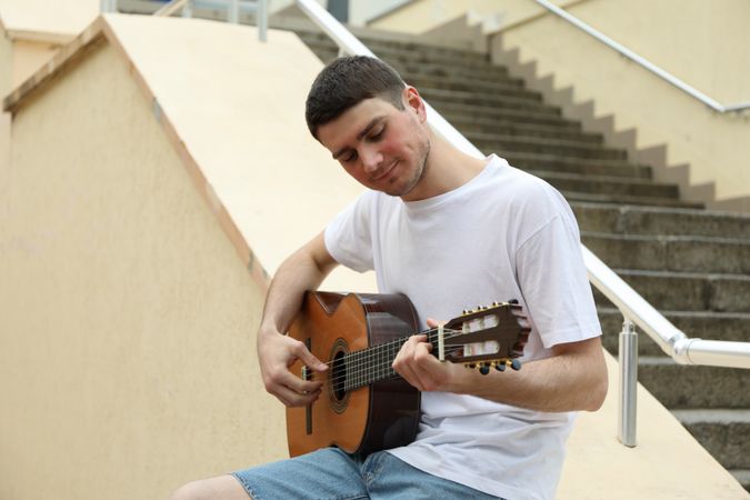 Young man in t-shirt sits and play on guitar