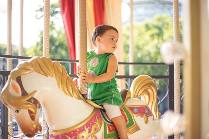 Curious little kid on colorful moving carousel at fair