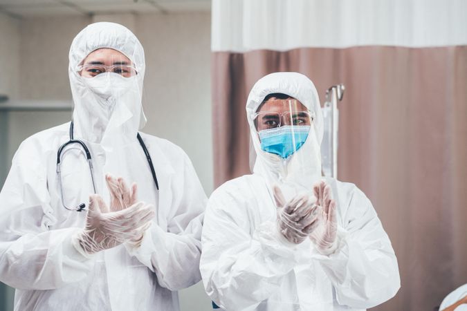 Two medical professional in full PPE clapping hands in celebration in emergency room