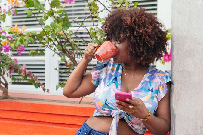 woman enjoying a coffee and looking at her cell phone on the street