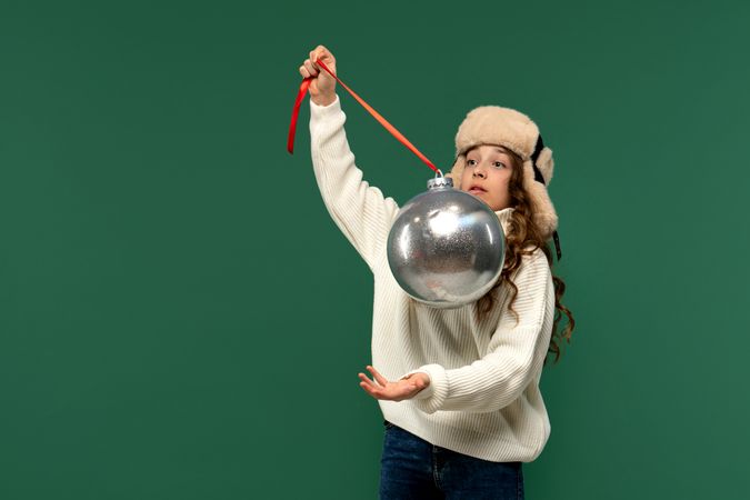 Surprised girl holding large silver Christmas ornament