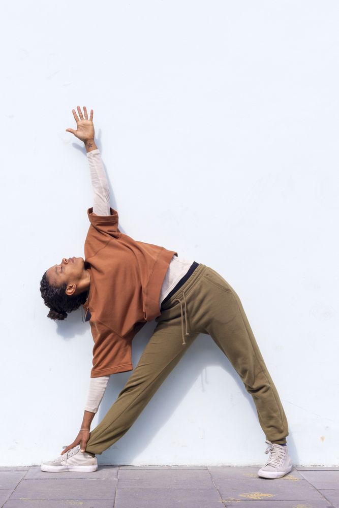 Stylish young female runner in athletic wear doing warm-up routine outdoors before running against wall