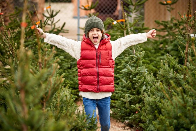 Excited boy raising arms near Christmas trees