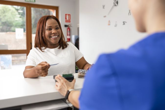 A Black woman smiles holding her credit card before paying after a dental visit
