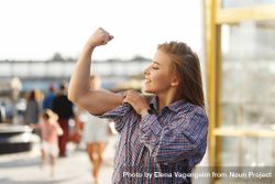 Smiling woman stands on the street curling her bicep 0WBGPb