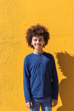 Black boy with curly hair standing on yellow wall