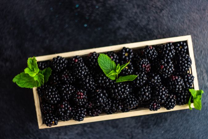 Top view of fresh raw blackberries in wooden box on stone background with copy space