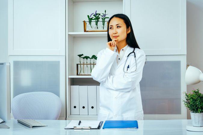 Asian doctor thinking about something in her office with her hand to her chin