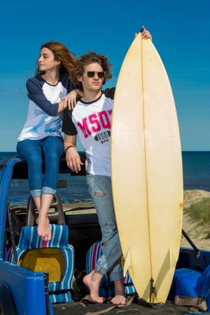 Guy with surfboard and woman on roof of car