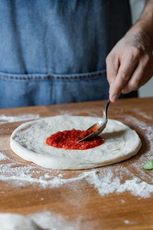 Crop man spreading sauce on pizza dough