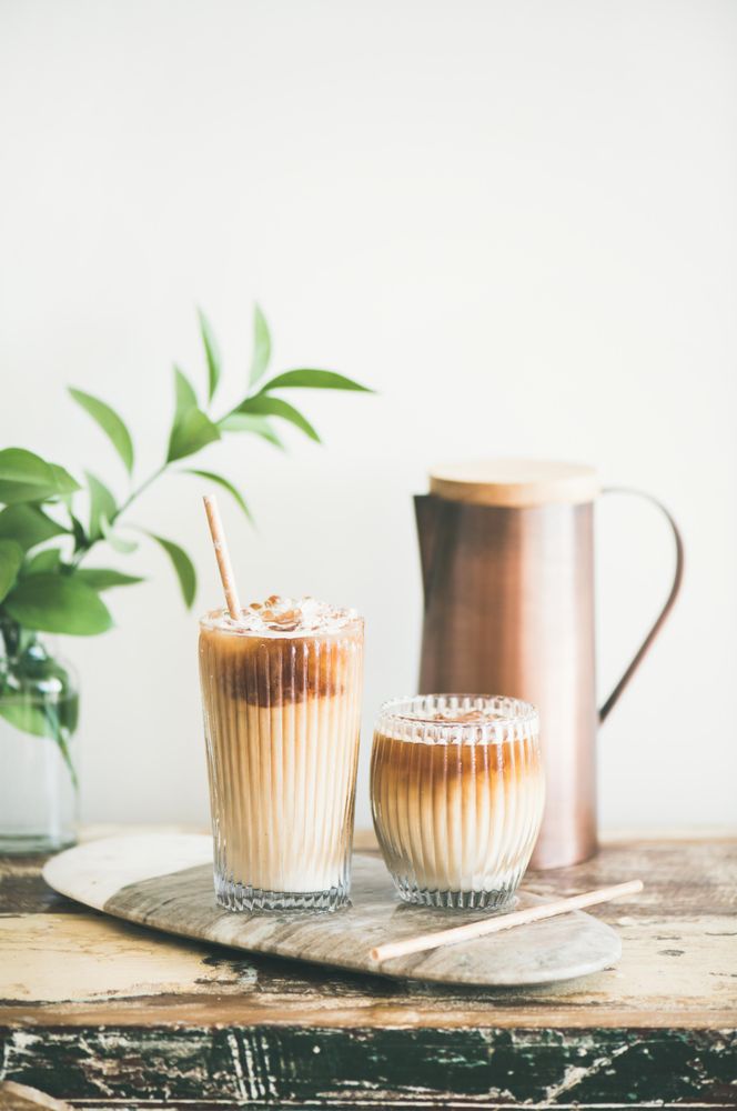 Two glasses of iced coffee and a pitcher, with light background with leaves