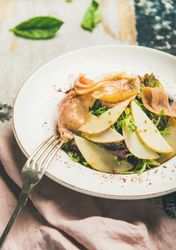Close up of ham and pear in bowl, with fork on linen napkin