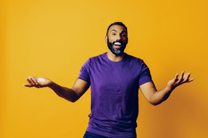 Black man smiling in yellow studio with open hands