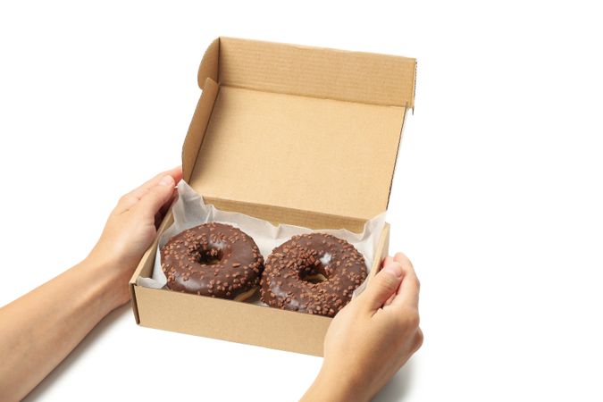 Female hands hold carton box with donuts, isolated on plain background