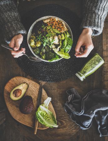 Healthy vegetarian bowl pictured on table with smoothie on side and hands with fork