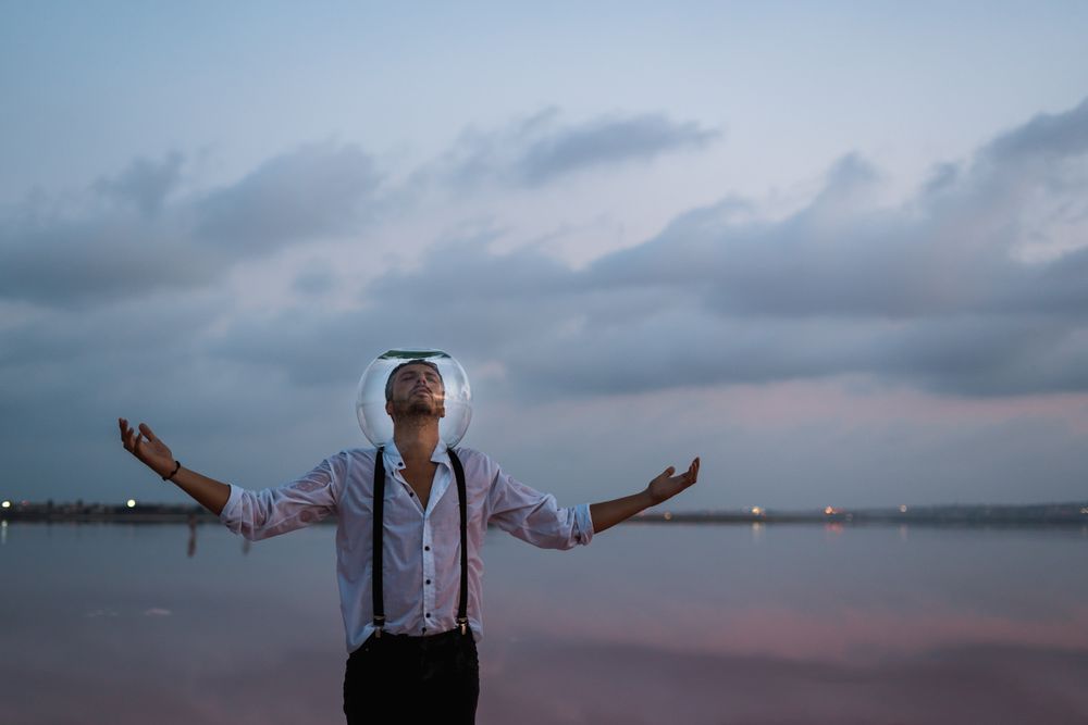 Man with fish tank on head standing at seashore