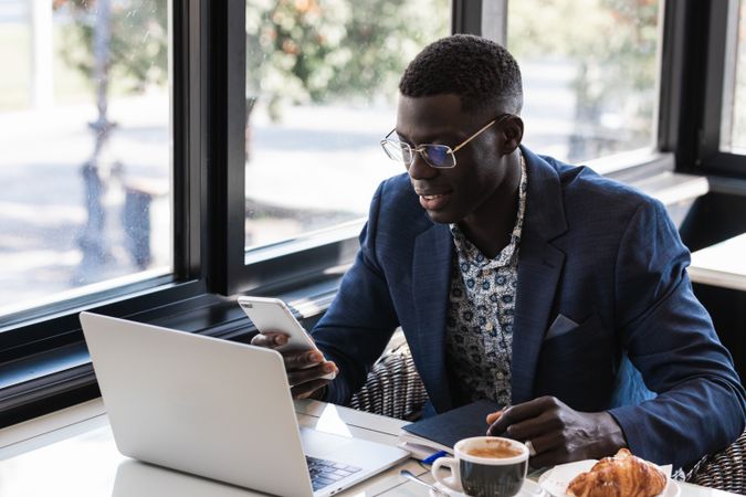 Stylish Black executive with smartphone and laptop in cafe