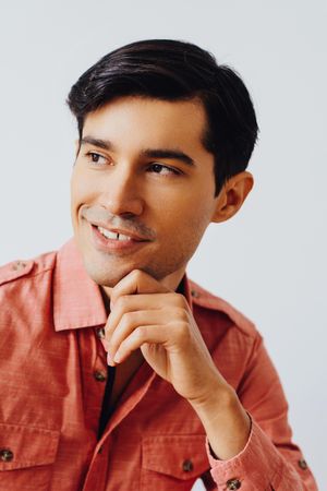 Headshot of happy Hispanic male looking away from camera in grey studio, vertical
