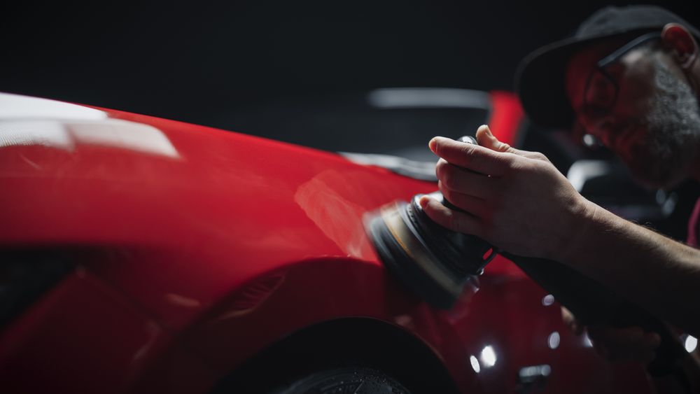 Adult Man Working in a Detailing Studio, Spreading Polishing Paste on a Fender of a Red Sportscar to Return it to Factory Condition.