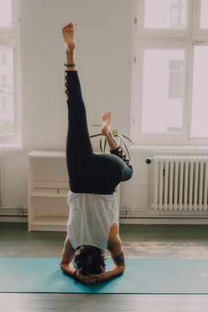 Fit woman practicing yoga pose and standing on head at home