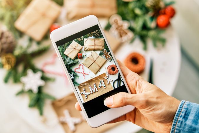 Faceless person photographing Christmas gifts on smartphone