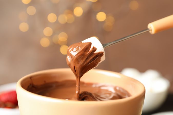Marshmallow in chocolate against brown background with blurred lights