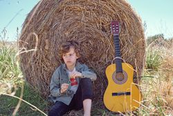 Upset kid sitting near guitar and leaning on hay bale