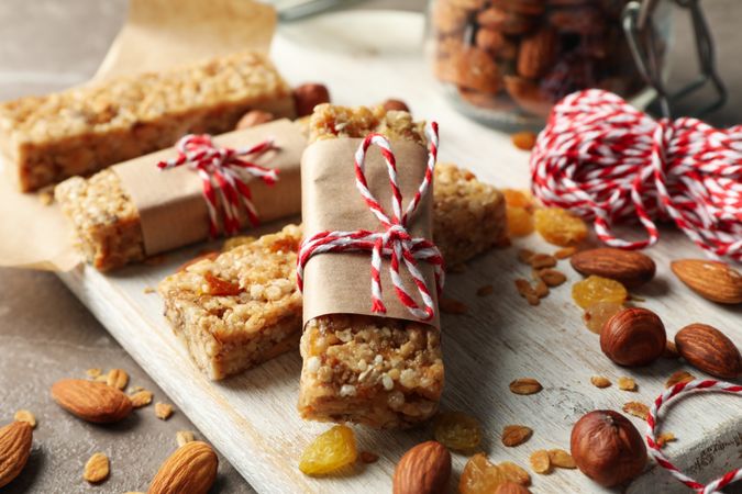 Board with tasty granola bars and nuts on gray background, close up