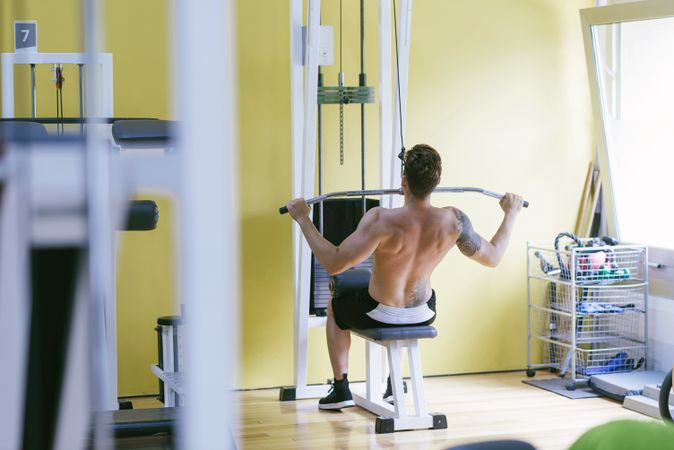 Tattooed male exercising his arms and chest on pull down machine