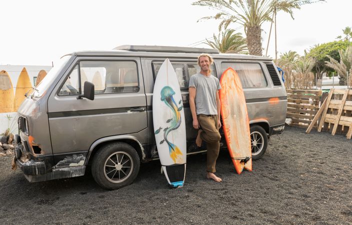 Smiling man standing near surf boards and van