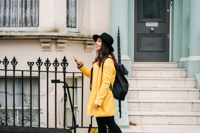 Stylish woman using smartphone near house on street