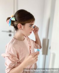 Young girl standing in front of the mirror applying mascara bEk7M5