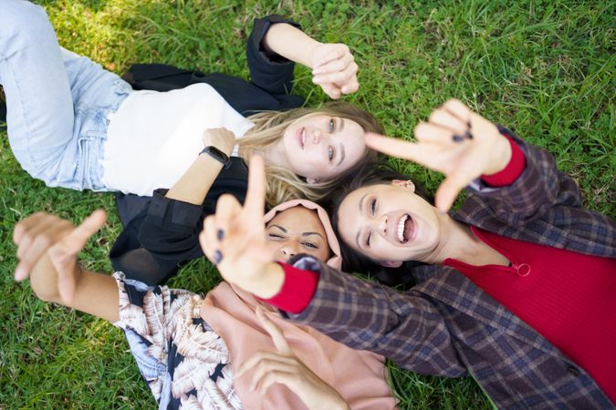 Looking down at three happy friends lying on grass smiling