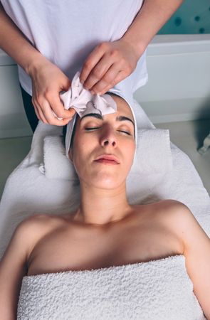 Female beautician removing clay facial mask from woman