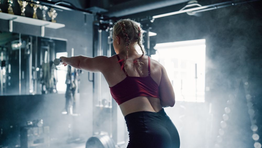 A Competitive Sportswoman Facing the Mirror While Training Using Dumbbells in a Dark Gym.