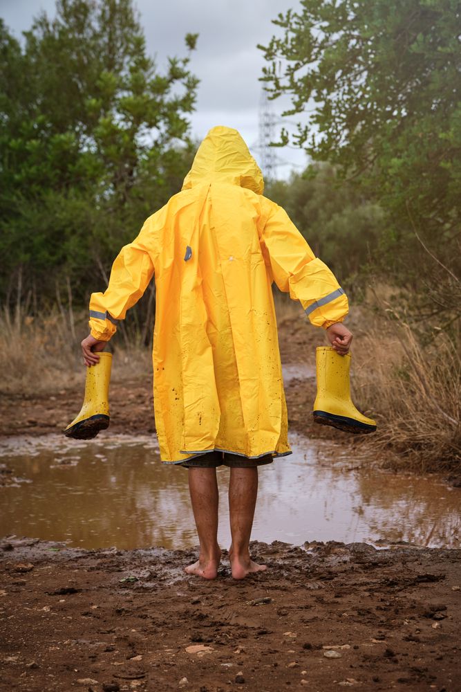 Barefoot kid with gumboots standing near puddle