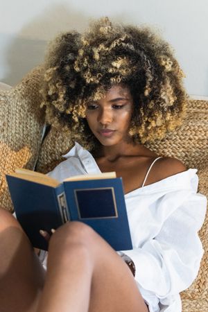 Young Black woman sitting on bed and reading book