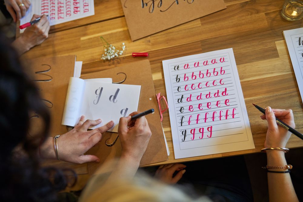 Crop faceless female students practicing lettering in classroom