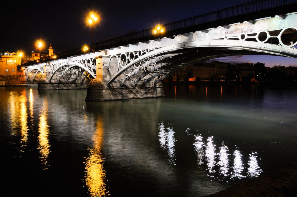 Triana Bridge over Guadalquivir river at sunset with reflections in the water