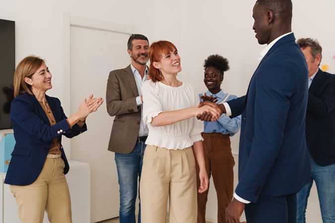 Diverse office colleagues clapping and shaking hands in celebration of a team member's success