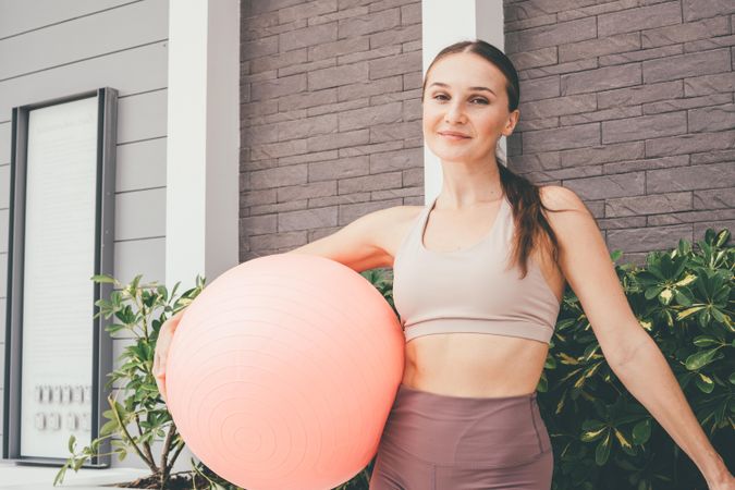 Woman standing outside with fitness ball in exercise clothes