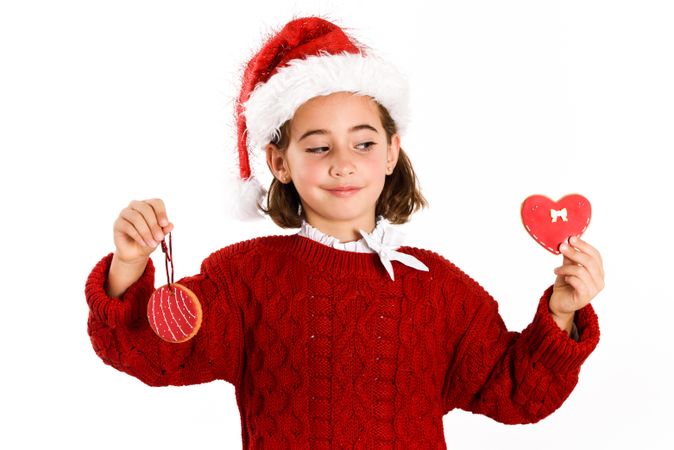 Female child in Christmas outfit holding up two red cookies