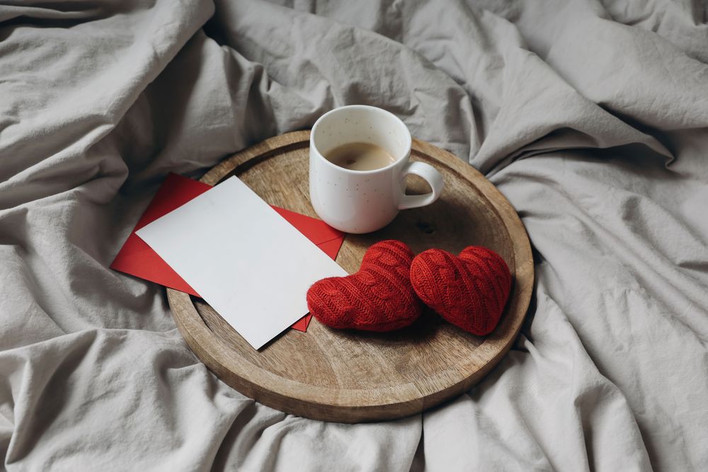 Red knitted hearts and cup of coffee on wooden plate.
