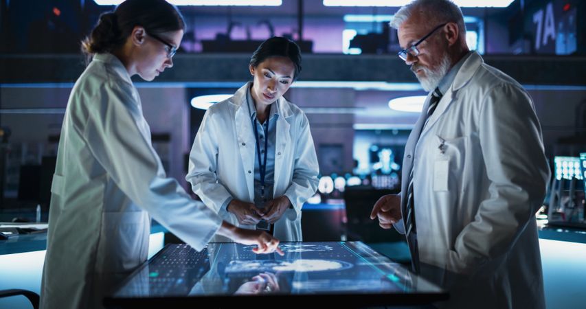 Modern Hospital Medical Research Center: Diverse Colleagues Gathered Around Interactive Touch Screen Table With MRI Scans Of Brain On Display.