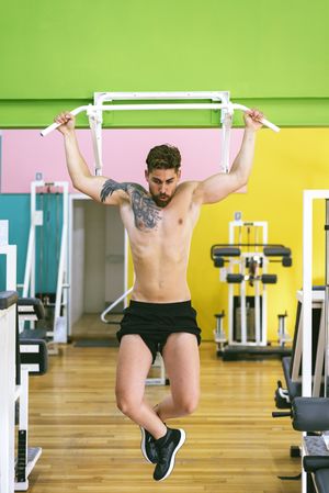 Front of man working out upper body in a fitness club on pull up bar