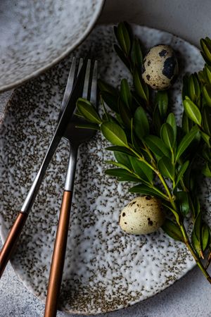 Easter card concept with close up of cutlery on elegant grey ceramic plates with branch and speckled eggs