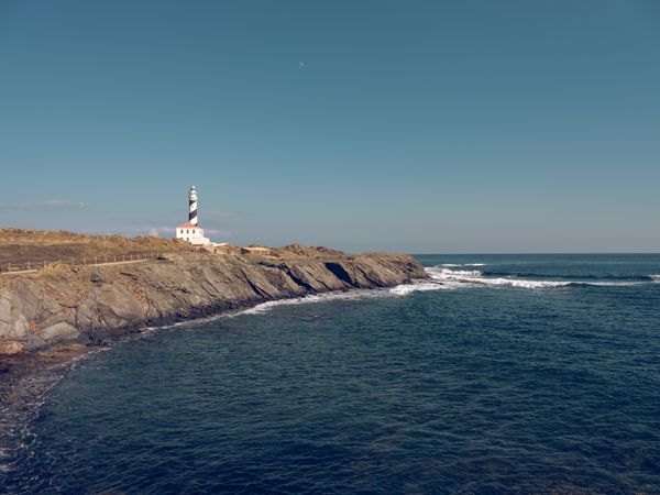 Lighthouse on rocky cliff in coast of turquoise sea
